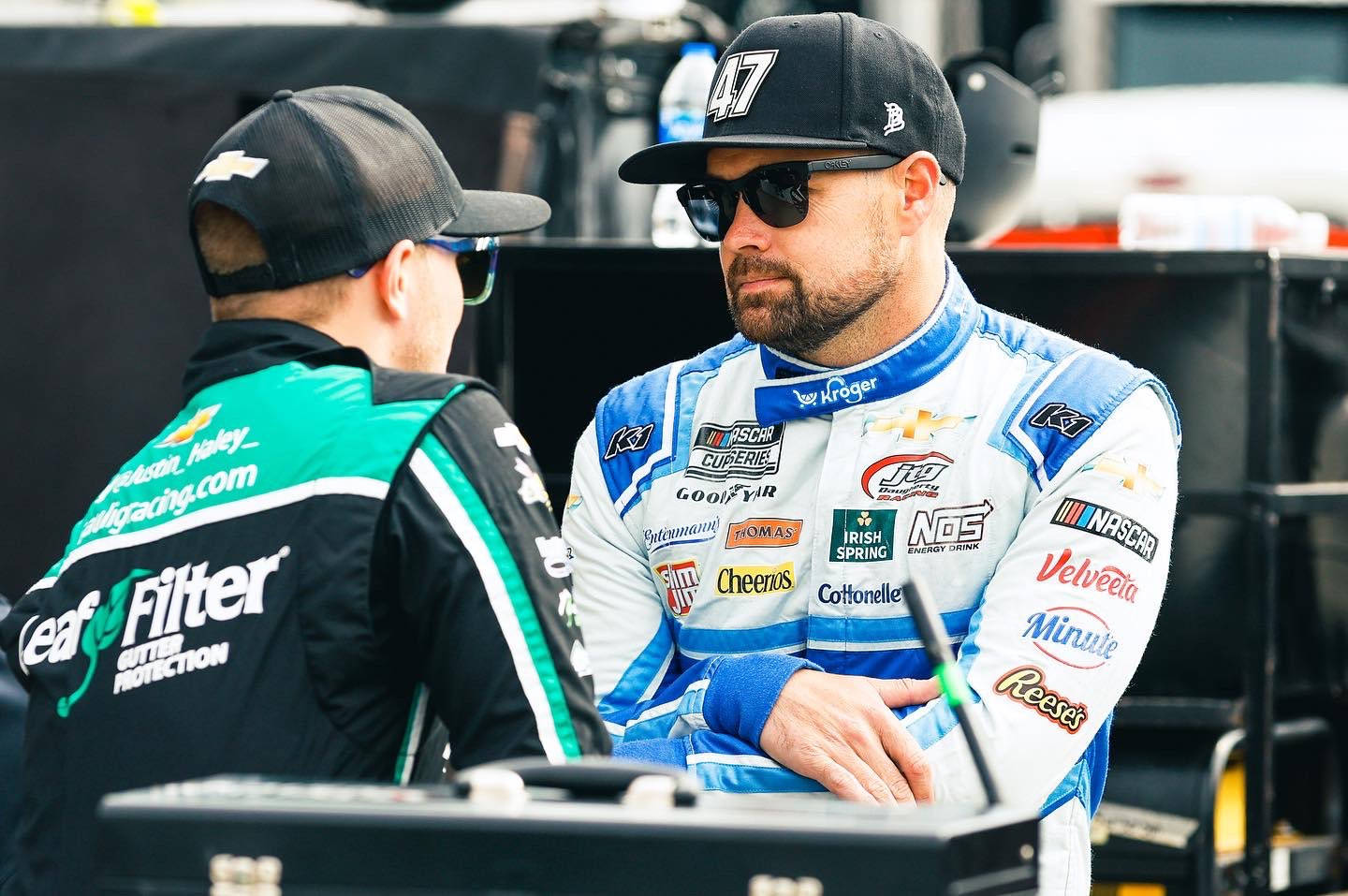 Men 桌布 壁紙 — NASCAR車手戴著太陽眼鏡和賽車服在維修區與工作人員交談。