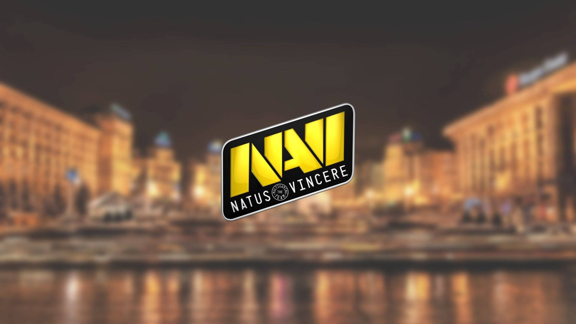 Natus Vincere 桌布 壁紙 — Natus Vincere 標誌在模糊的夜間城市景觀和水面上的溫暖倒影中，以鮮明的黃色發光。
