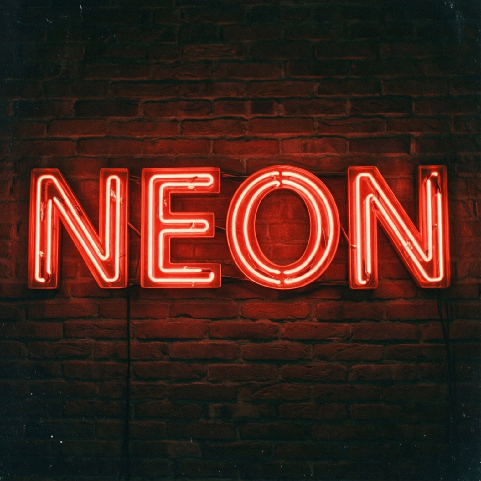 霓虹紅「NEON」招牌 壁紙 — 一個發光的紅色霓虹燈牌拼出NEON，在陰暗的城市環境中，將溫暖的光線投射在深色磚牆上。