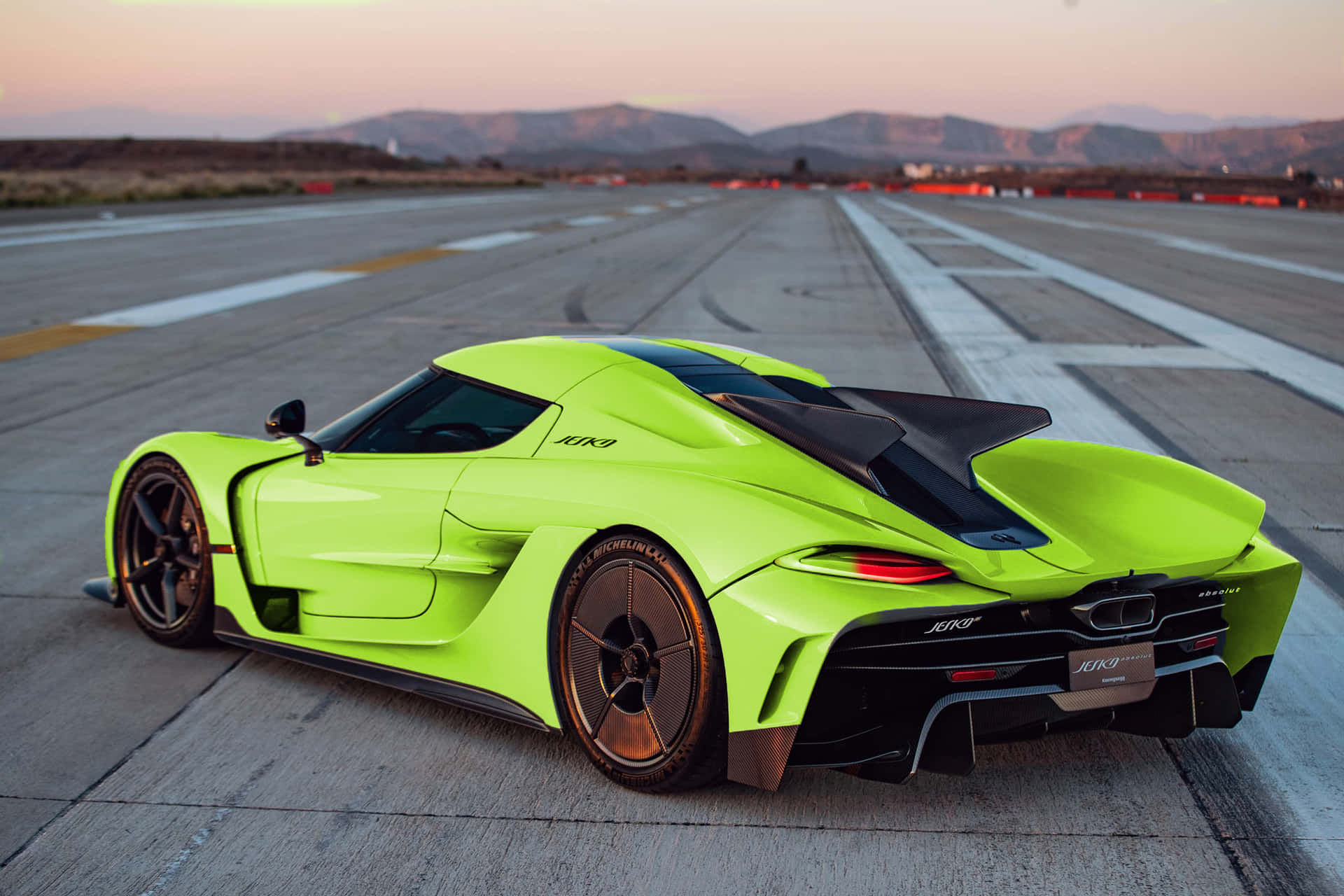  壁紙 — 一輛螢光綠色的Koenigsegg Jesko hypercar停在空曠的跑道上，日落時分，遠山如黛。
