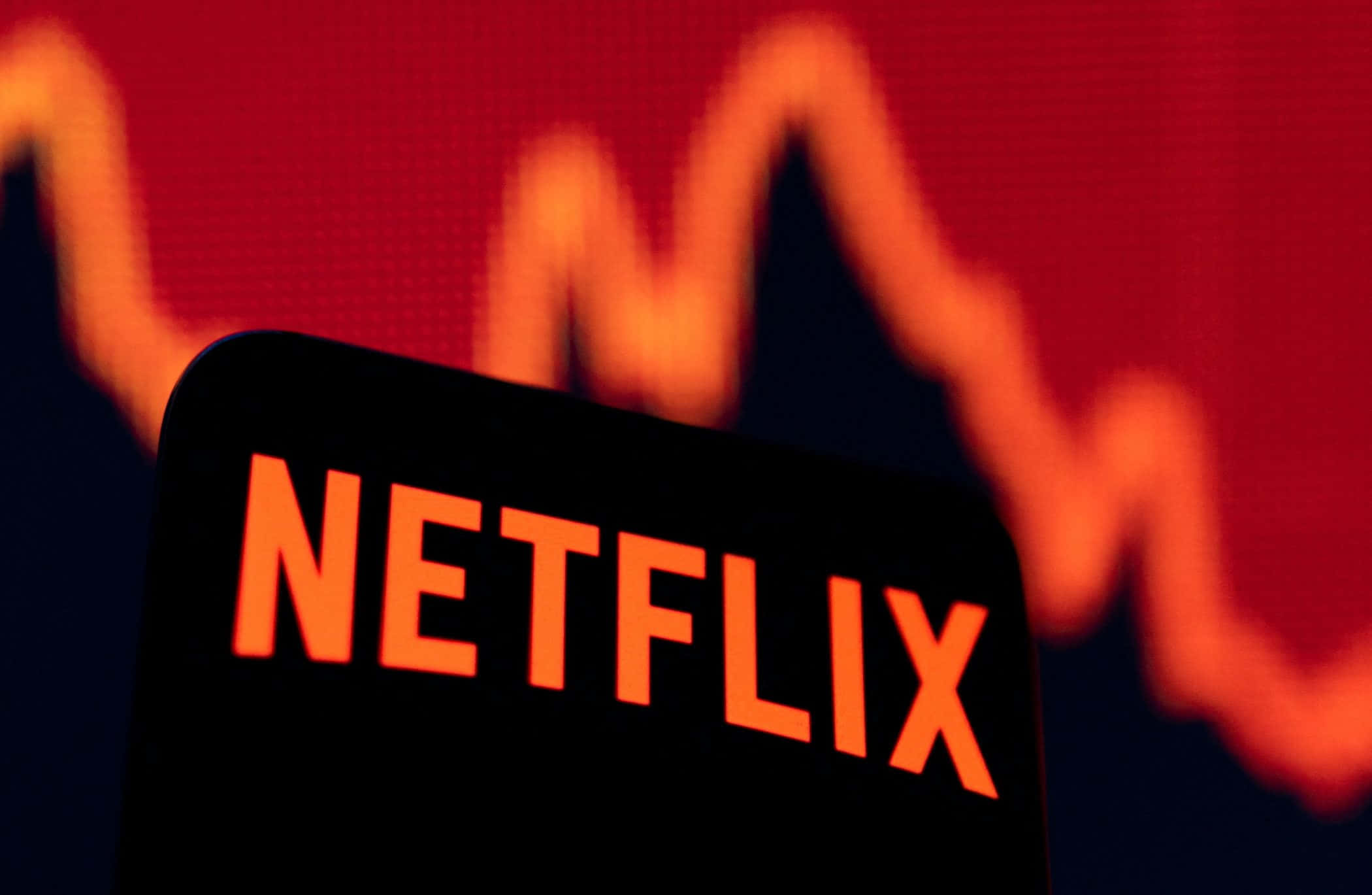 Netflix 桌布 壁紙 — Netflix 標誌的特寫，在模糊的紅色股票圖表背景上發出橙色光芒。