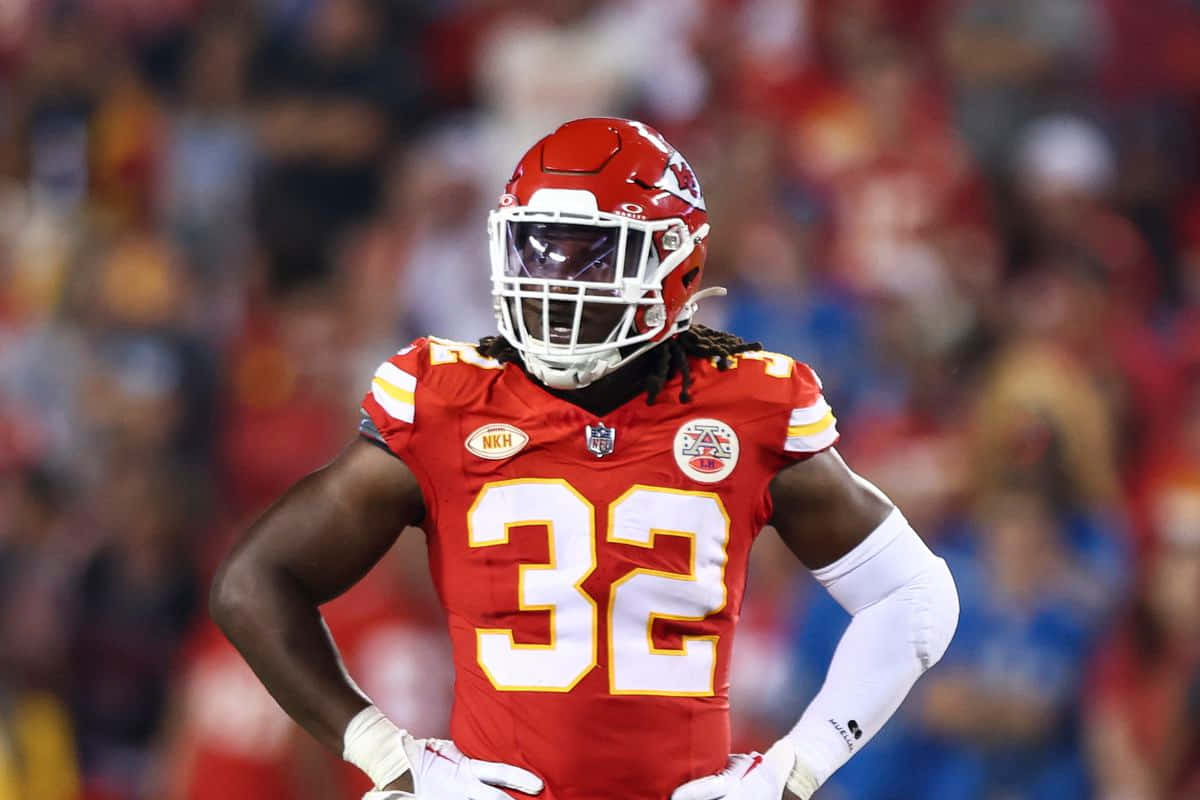 壁紙 — 一位專注的NFL美式足球員身穿紅色32號球衣，雙手叉腰站在燈光明亮的球場上。