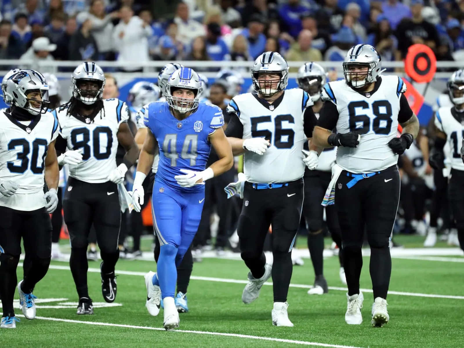  壁紙 — NFL 美式足球員身穿藍白球衣，在球場燈光下於綠色場地上衝刺。