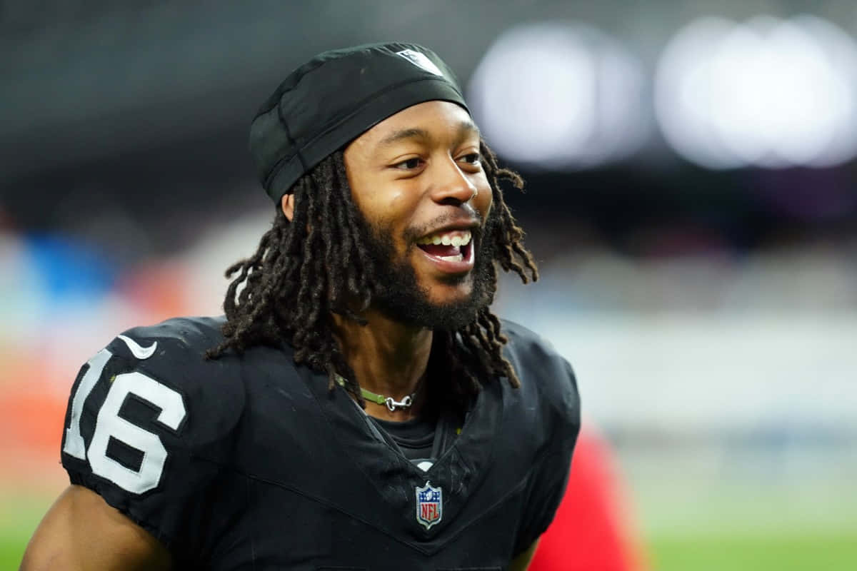 壁紙 — 一位面帶微笑、梳著辮子、身穿黑色球衣16號的NFL美式足球員，在球場燈光下比賽時大笑。