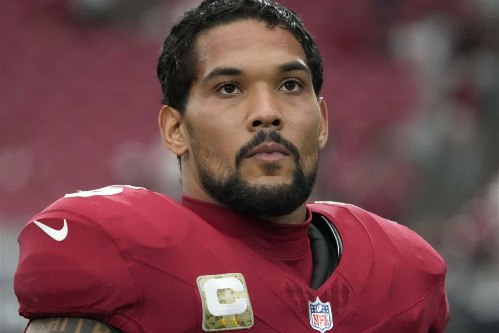  壁紙 — 一位身穿紅色球衣、帶有隊長臂章的NFL球員，在球場燈光下的比賽中專注地凝視。