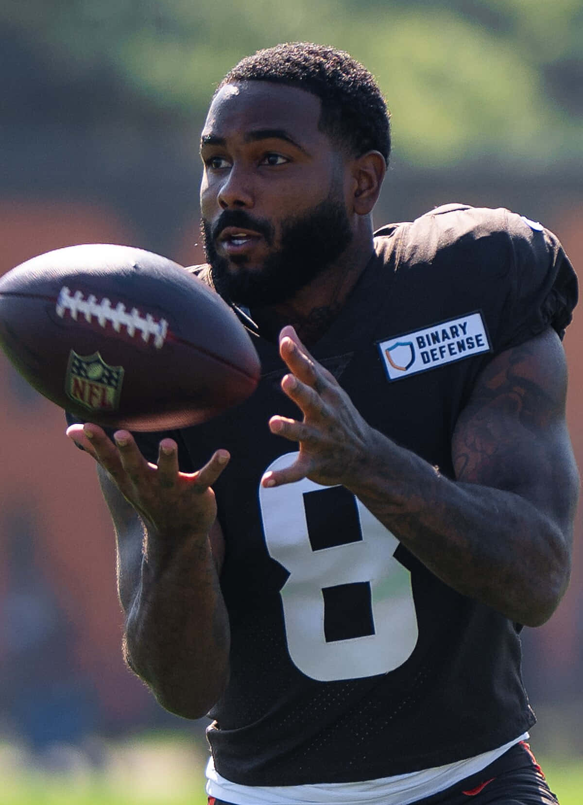  壁紙 — 一位專注的NFL四分衛身穿黑色8號球衣，在陽光明媚的戶外訓練中準備傳球。