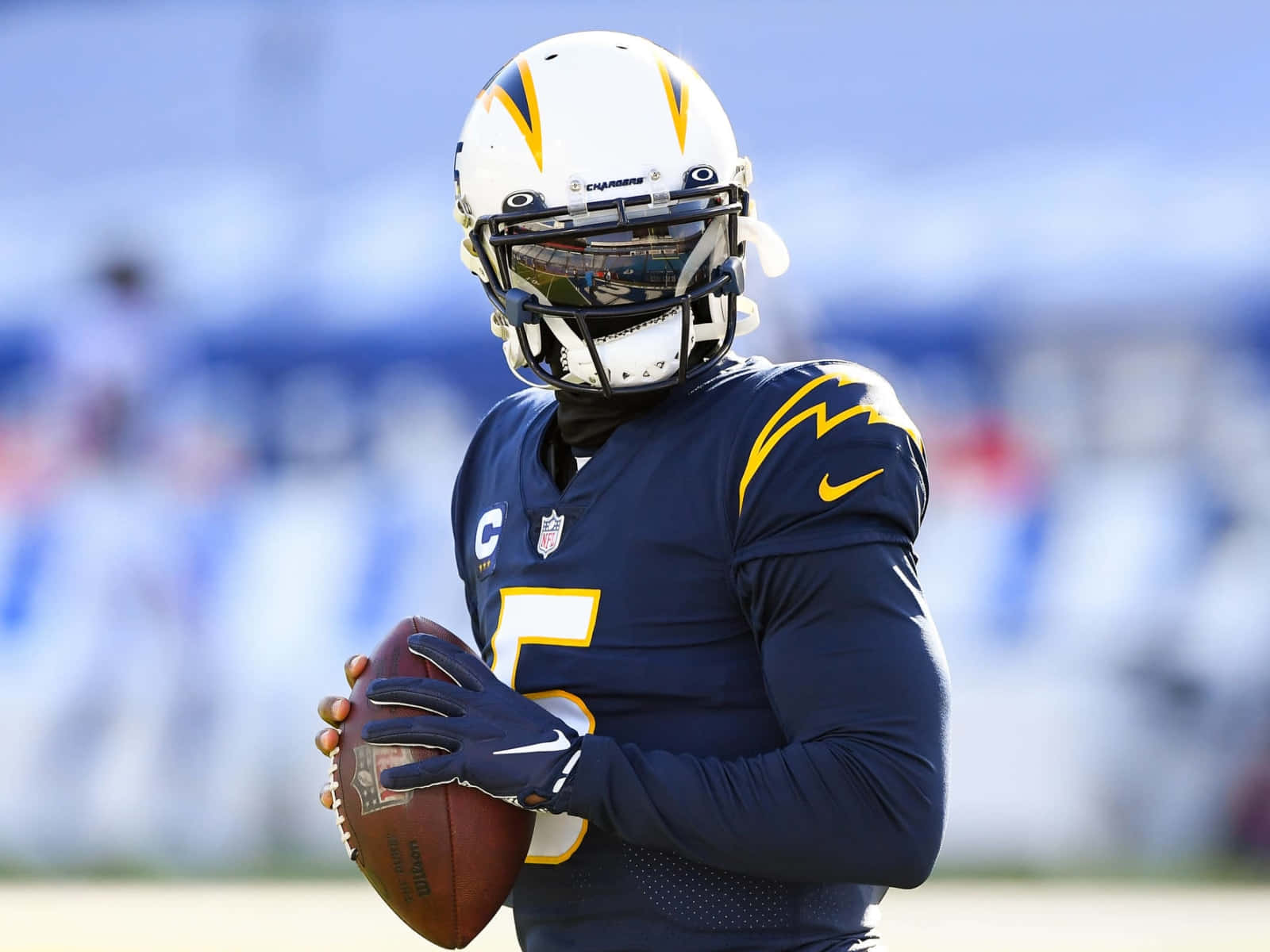  壁紙 — 一位專注的NFL四分衛穿著電光隊球衣，在明亮的日光下於球場上抱著美式足球。