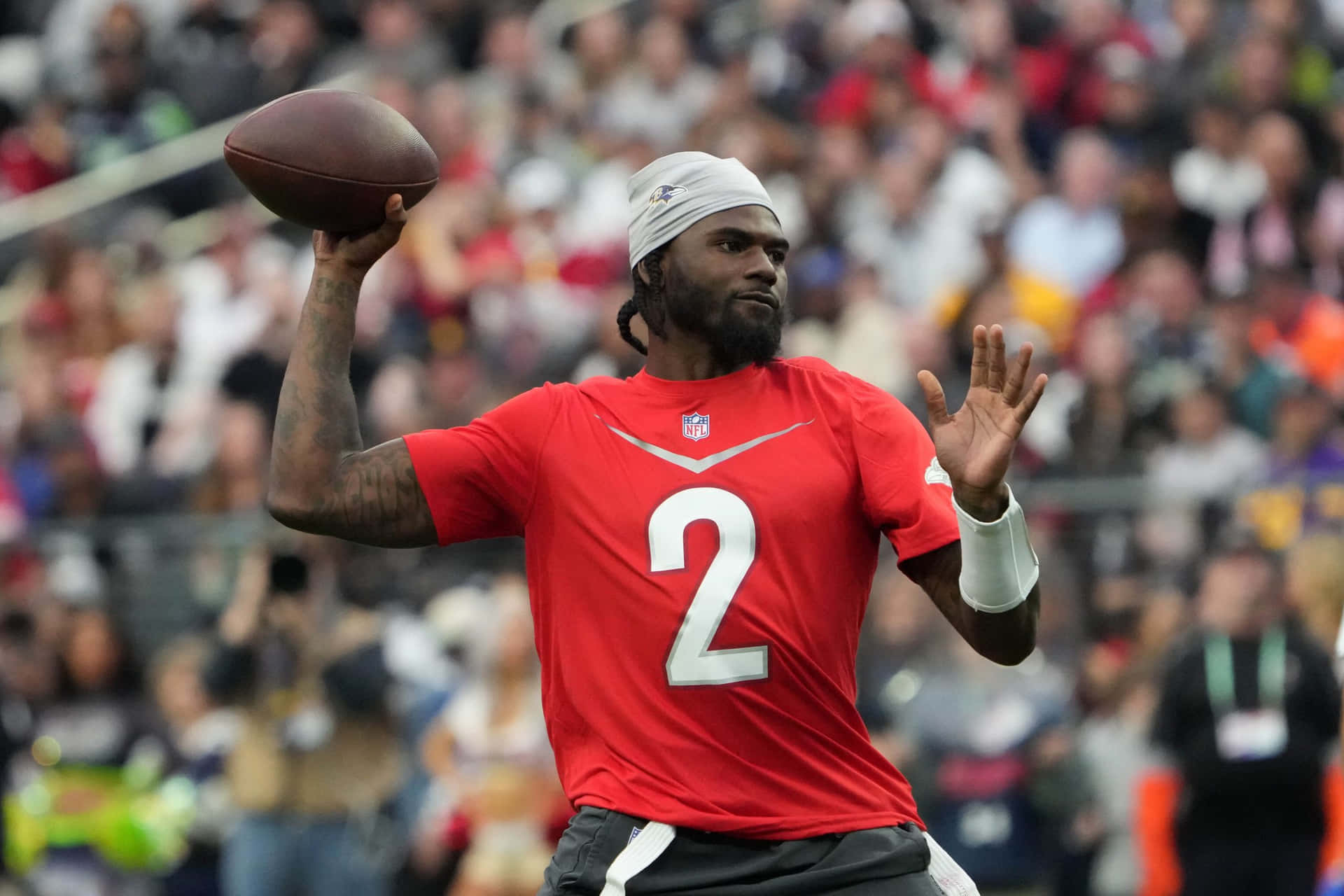  壁紙 — 一位專注的NFL四分衛身穿紅色球衣背號二，在白天比賽中準備擲出橄欖球，背景是模糊的人群。
