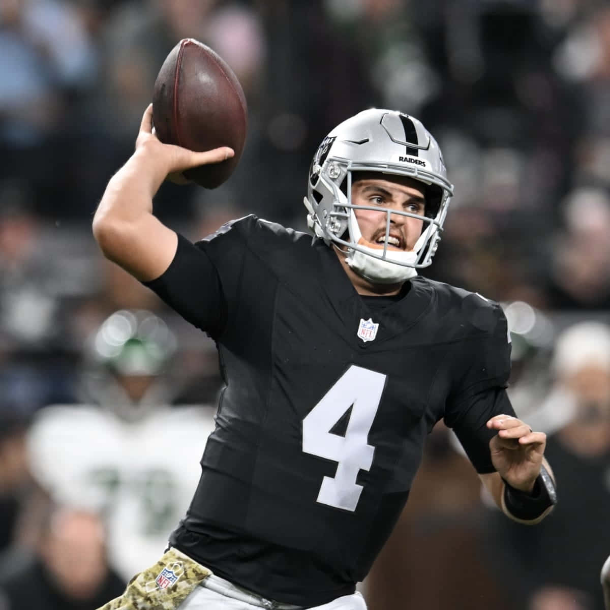  壁紙 — 一位專注的NFL四分衛，身穿黑色Raiders球衣，背號4，在夜間比賽中準備擲出橄欖球。