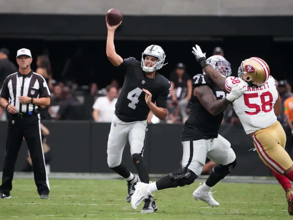  壁紙 — 一位身穿黑色球衣的NFL四分衛擲出橄欖球，而一位身穿白色和金色的防守球員衝上前進行擒抱。