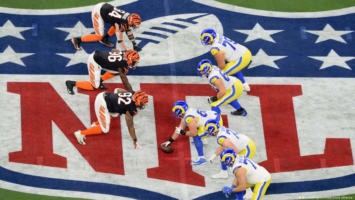 NFL 桌布 壁紙 — NFL 球員身穿黑色、橙色和藍白相間的球衣，在帶有巨大紅色 NFL 標誌和星星的場地上爭奪球權。
