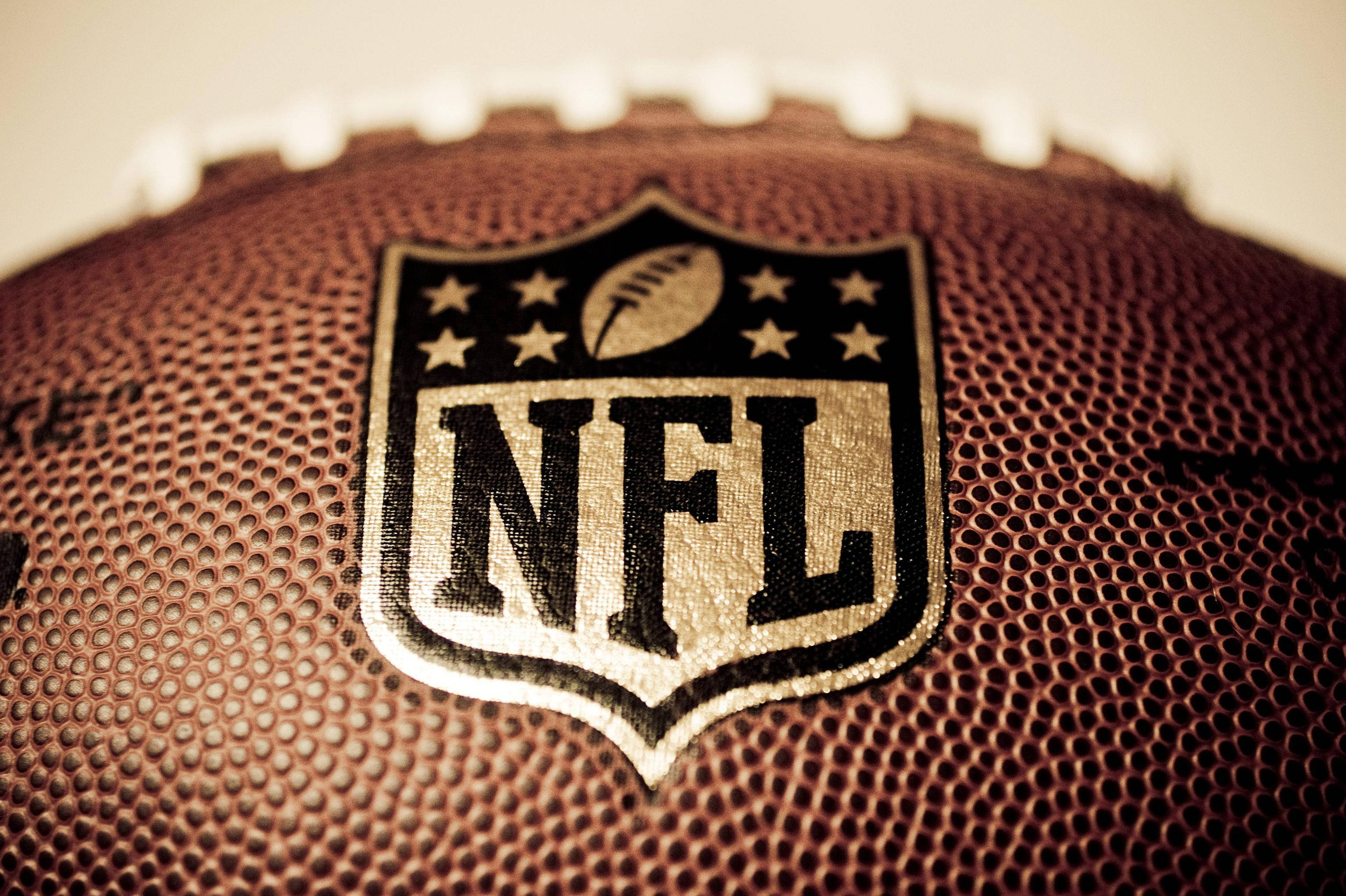 NFL 美式足球 桌布 壁紙 — NFL 美式足球特寫，帶有紋理皮革和標誌性標誌，呈現溫暖的棕褐色調。