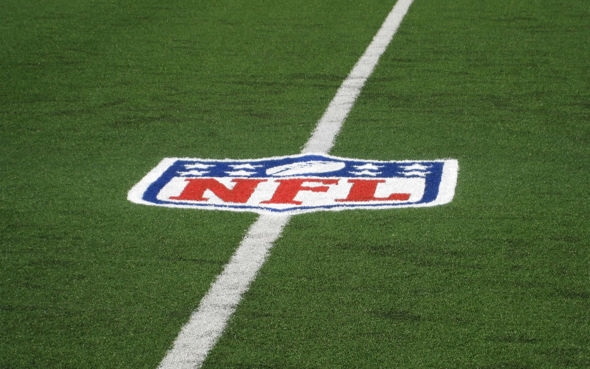 NFL 桌布 壁紙 — NFL標誌的特寫，繪在充滿活力的綠色草皮上，並有一條清晰的白色碼線與之交錯。