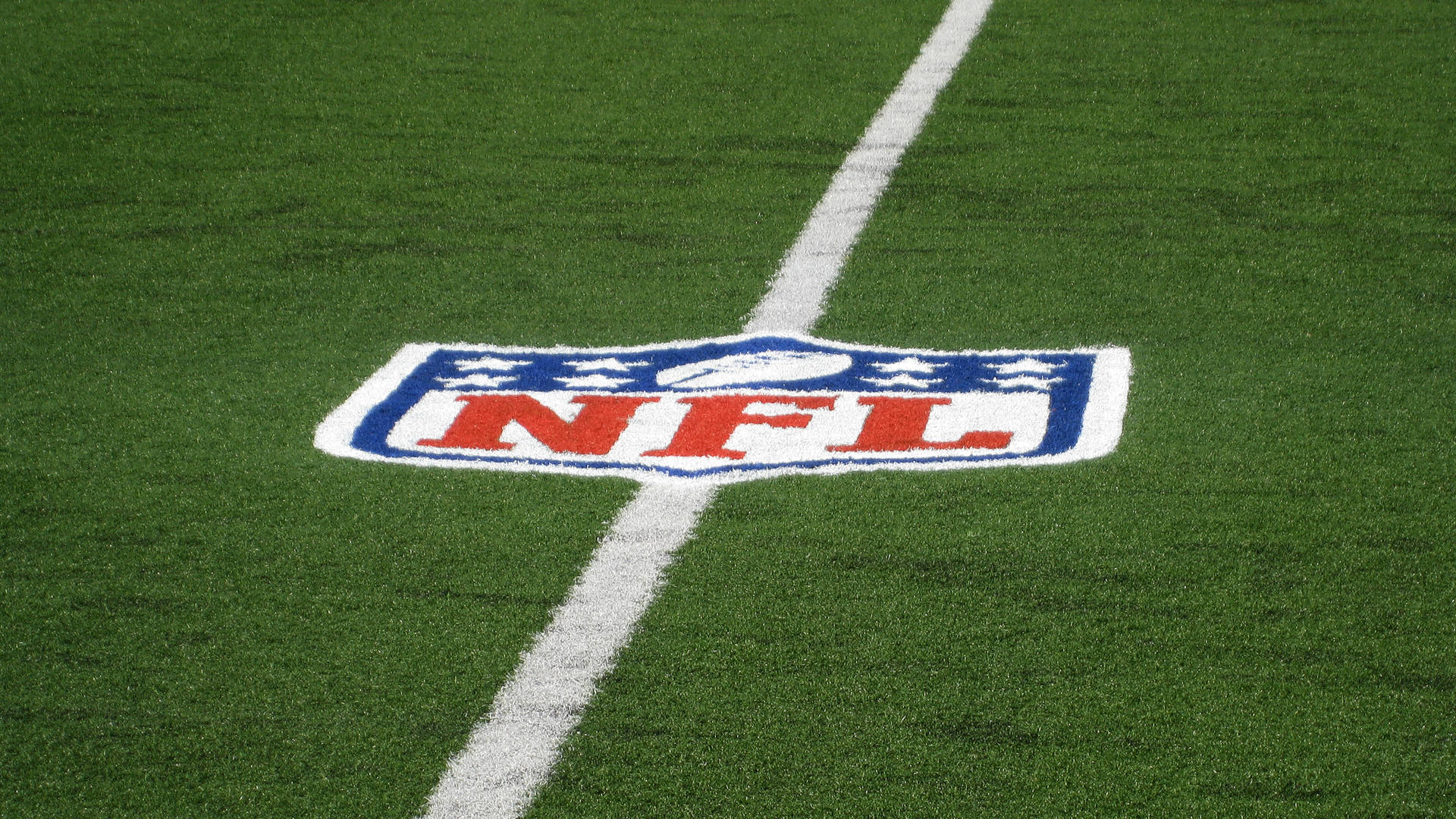 NFL 桌布 壁紙 — NFL標誌的特寫，繪在充滿活力的綠色草地上，被一條清晰的白色碼線穿過。