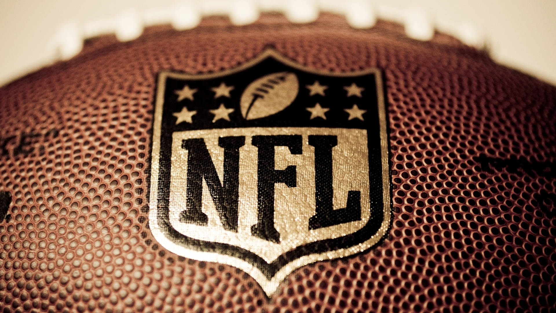 NFL 桌布 壁紙 — NFL標誌近距離特寫，縫在棕色皮革橄欖球上，可見鞋帶和紋理表面。