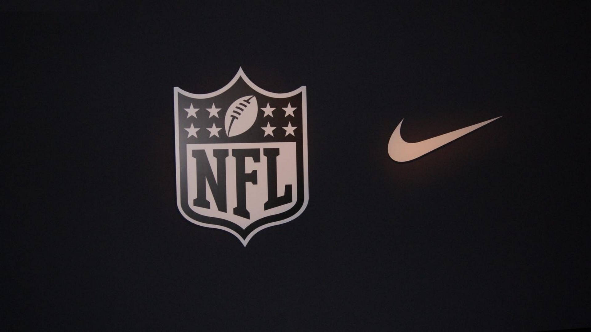 NFL 桌布 壁紙 — NFL盾牌標誌和Nike勾勾在深色背景上柔和發光。