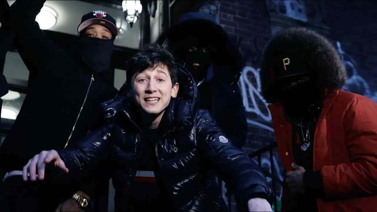  壁紙 — 一位穿著黑色羽絨外套的年輕男子對著鏡頭微笑，而三個戴著面具的人影在夜晚站在他身後，背景是塗鴉覆蓋的城市小巷。
