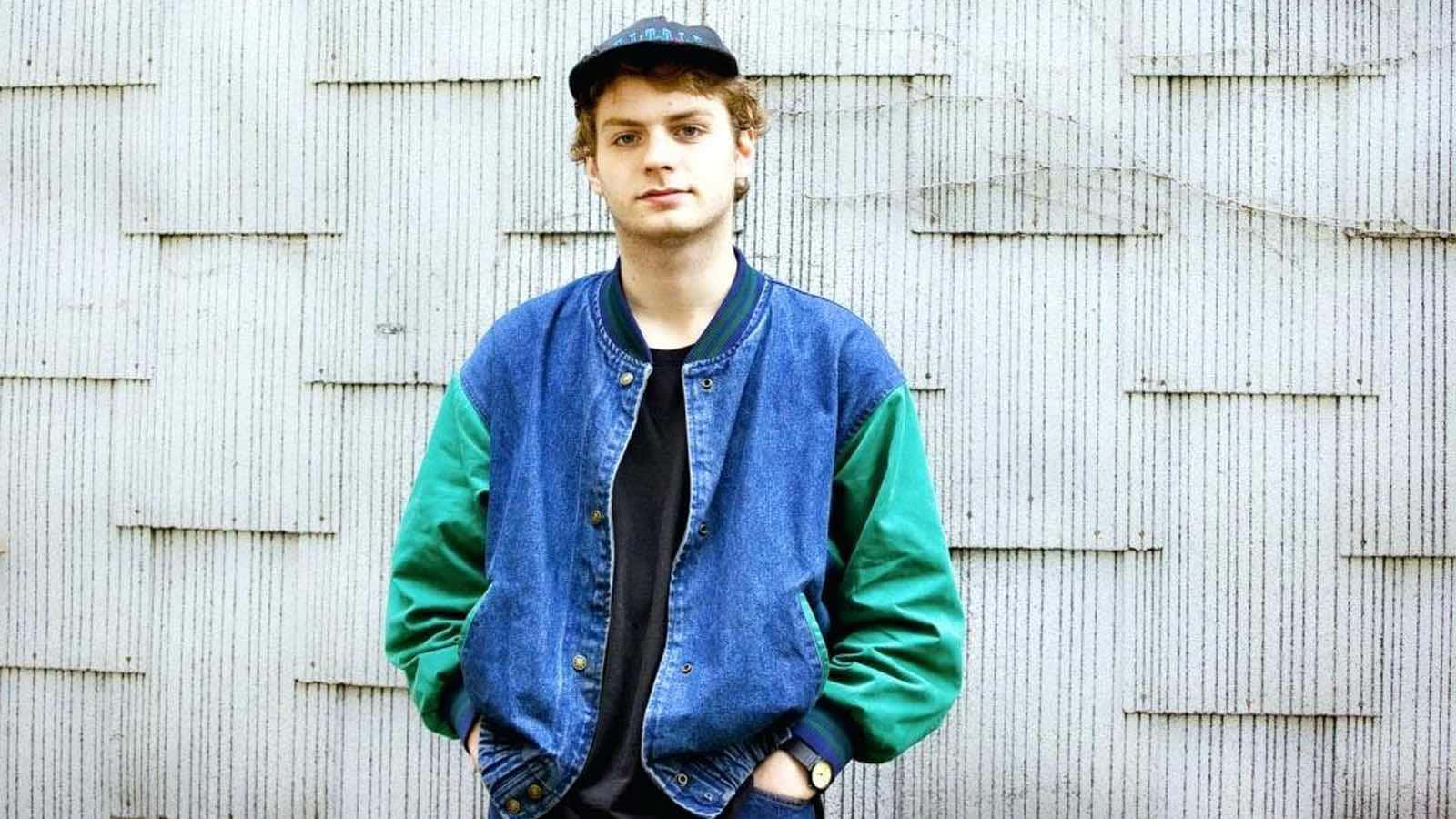  壁紙 — 一位身穿藍綠色牛仔外套和帽子的年輕男子自信地靠在一面風化的木牆上。