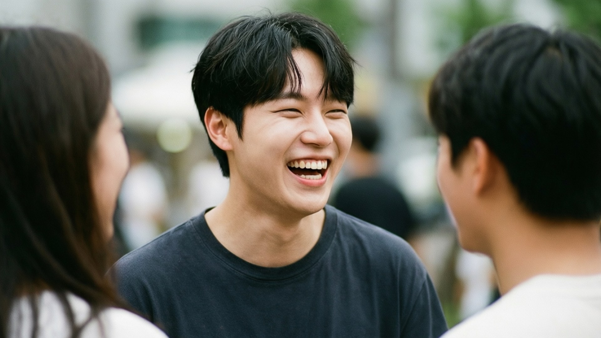 Candid Laughter 壁紙 — 一位年輕男子在明亮的城市街道上與兩位朋友聊天時開懷大笑。