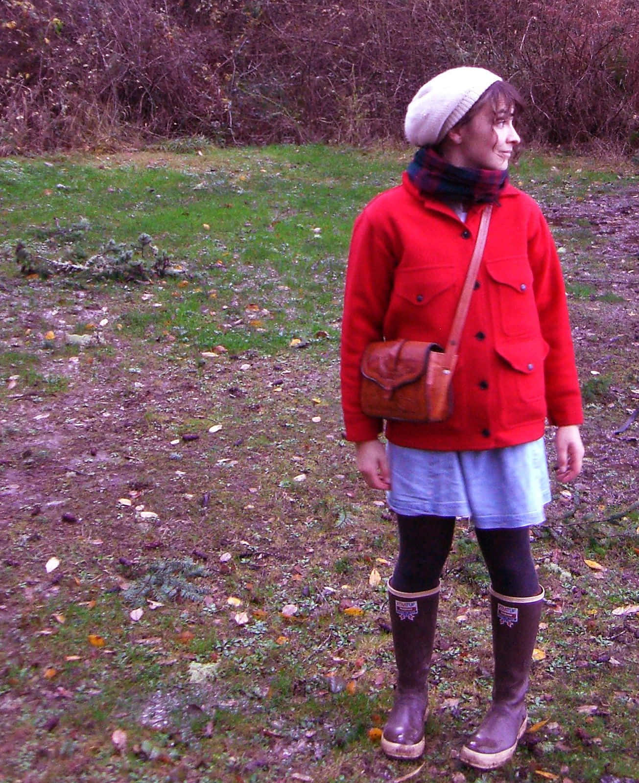 Red Coat 桌布 壁紙 — 一位年輕女性身穿亮紅色外套和棕色靴子，站在散落著落葉的草地上微笑。
