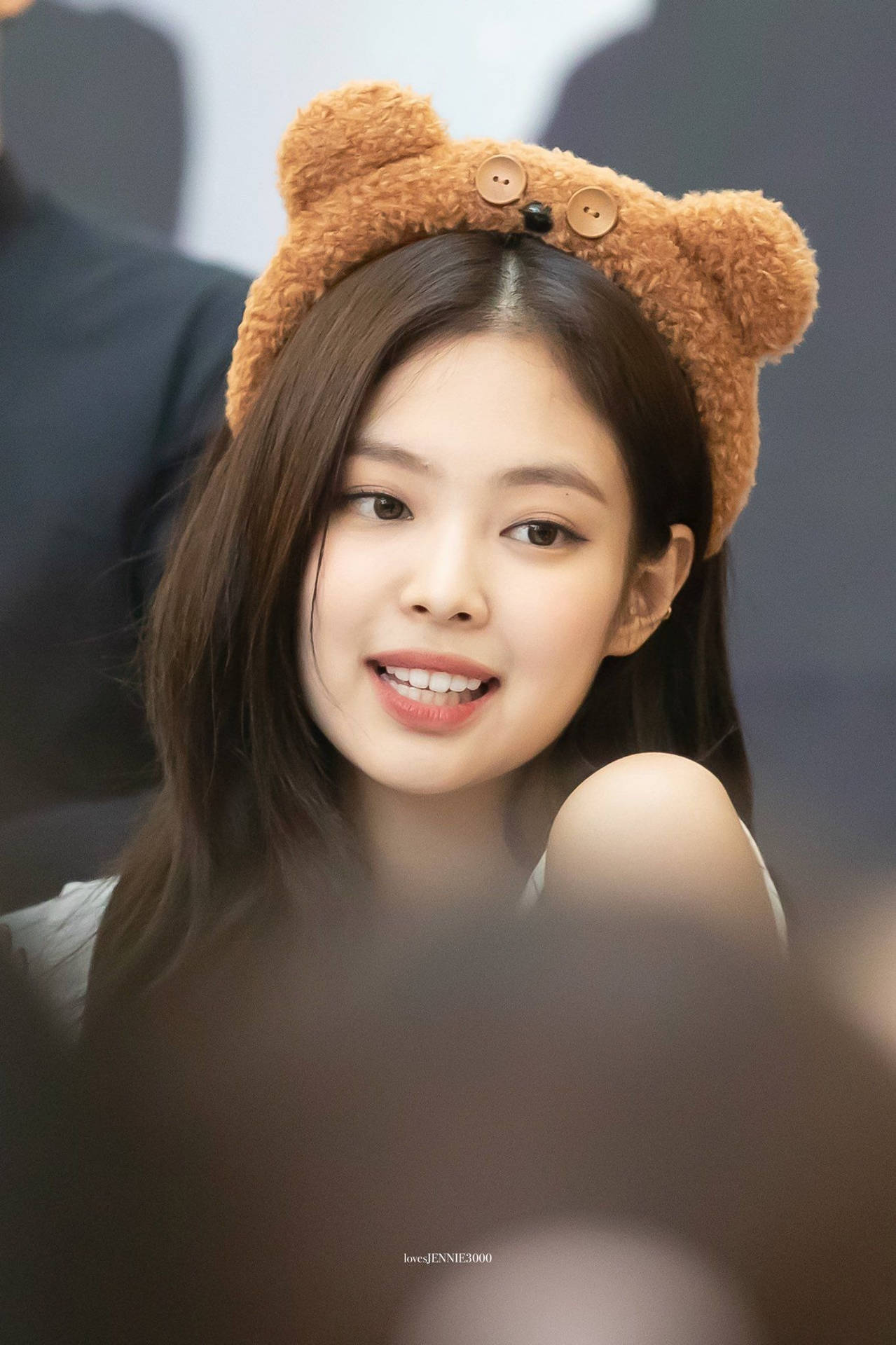 戴著棕色熊耳頭帶並輕柔微笑的年輕女性。 — Jennie 壁紙