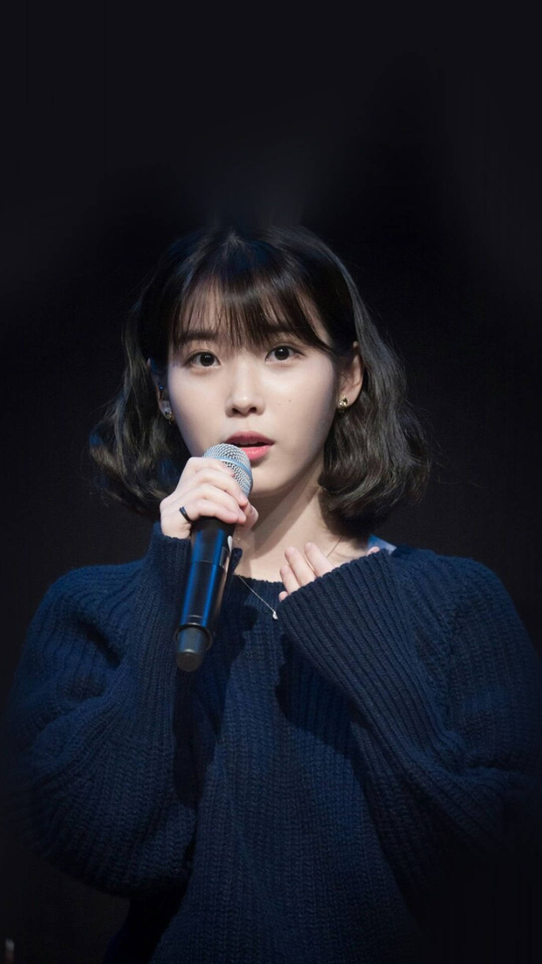 年輕女性身穿海軍藍毛衣在舞台上手持麥克風 — K Pop 壁紙