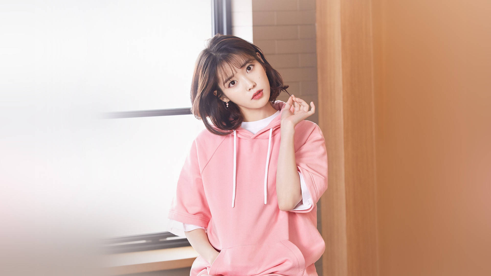 年輕女子粉紅連帽衫靠木門窗光 — K Pop 壁紙