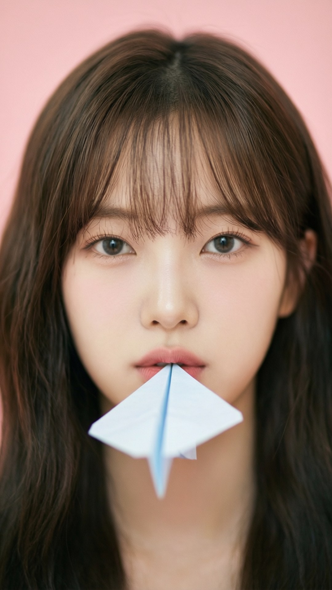 Jiho Dreamy Portrait 壁紙 — 一位深色頭髮的年輕女子在柔和的粉紅色背景前，將白色紙飛機放在唇邊。