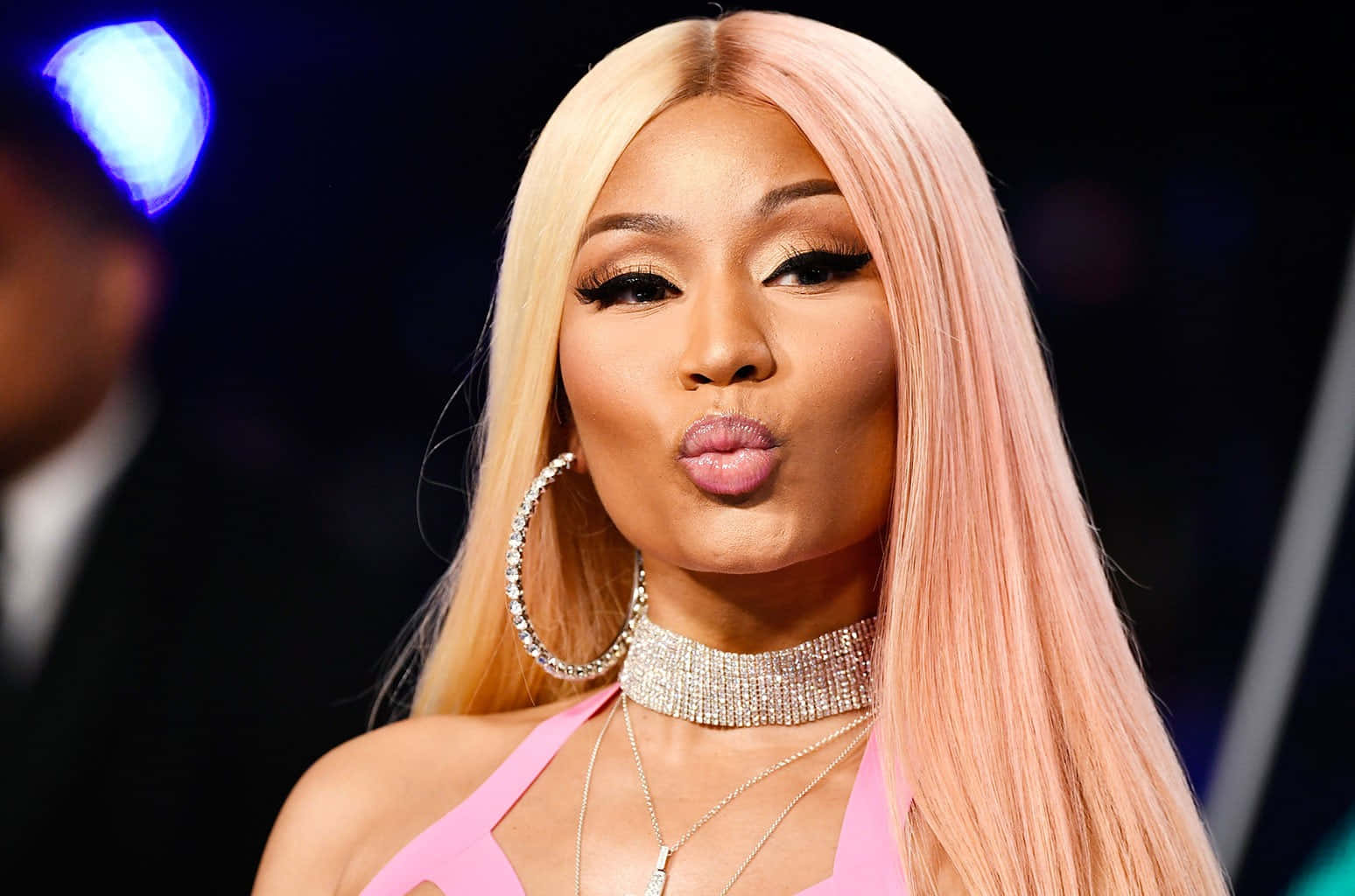 妮琪·米娜 桌布 壁紙 — Nicki Minaj 留著粉紅色頭髮，佩戴鑽石珠寶，在舞台燈光下的華麗活動中嘟起嘴唇。