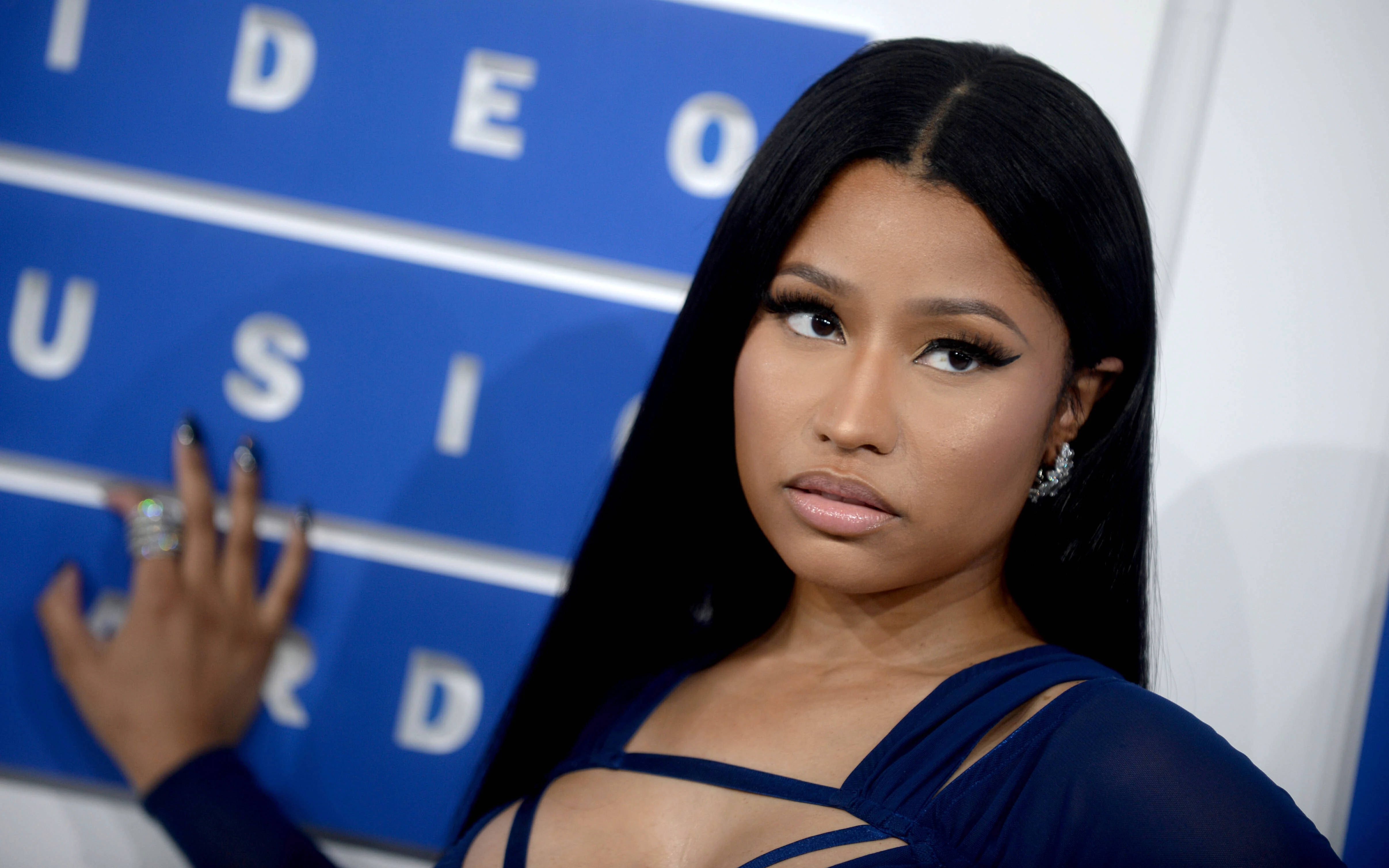 說唱歌手 桌布 壁紙 — Nicki Minaj 自信地穿著藍色連衣裙，在藍色「VIDEO MUSIC AWARD」背景前擺姿勢，背景上有粗體白色字樣。