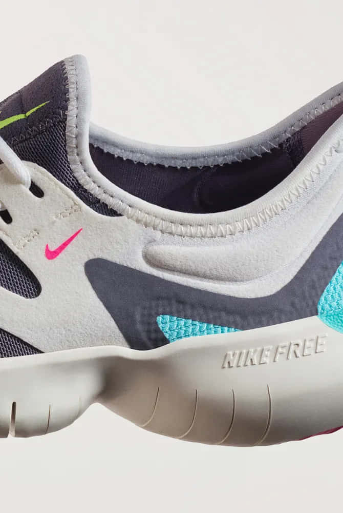 Nike 桌布 壁紙 — Nike Free 跑鞋特寫，展示灰色網眼鞋面、粉紅色勾勾和藍綠色點綴，背景中性。