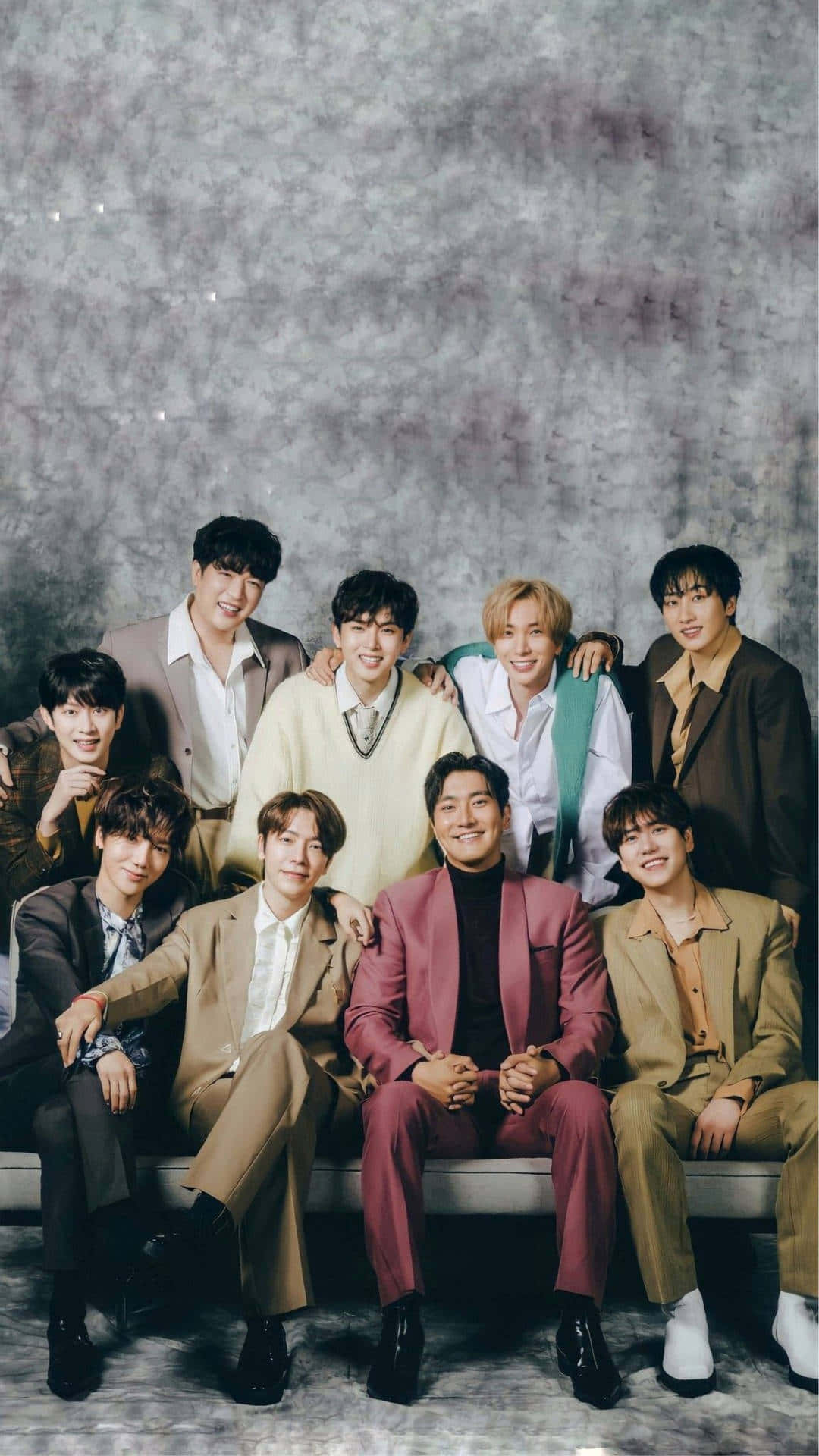 九位穿著時尚西裝的男士在攝影棚環境中於長椅上一起擺姿勢。 — K Pop 壁紙