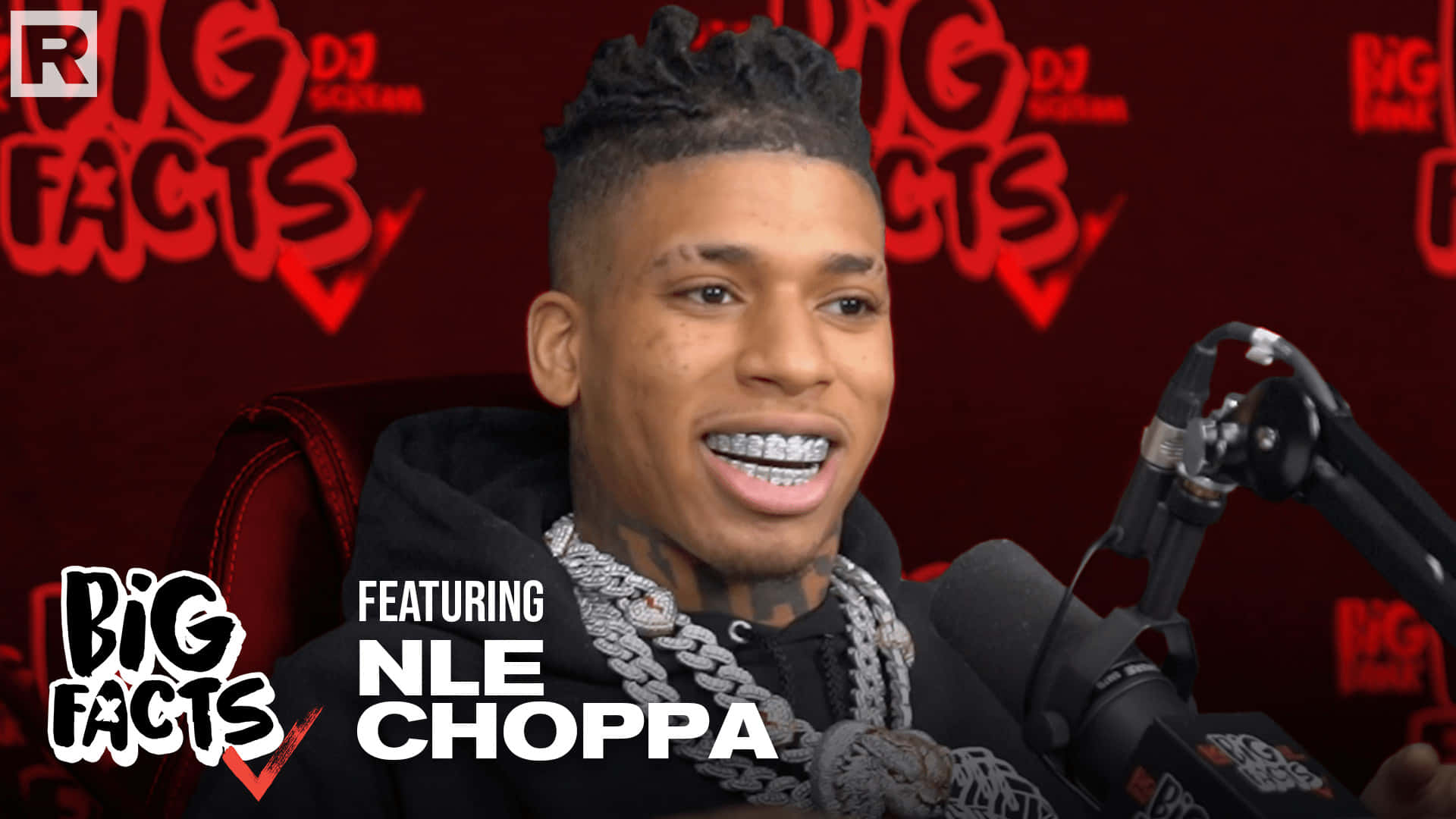 NLE Choppa 桌布 壁紙 — NLE Choppa 戴著 grillz 坐在紅色 'Big Facts' 品牌背景前，露出燦爛笑容。