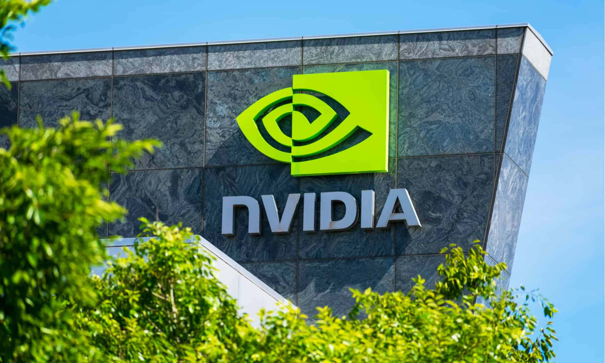nvidia 桌布 壁紙 — NVIDIA 企業建築，亮綠色標誌和銀色字體在深色石牆上，周圍環繞著茂密的綠樹，天空清澈湛藍。