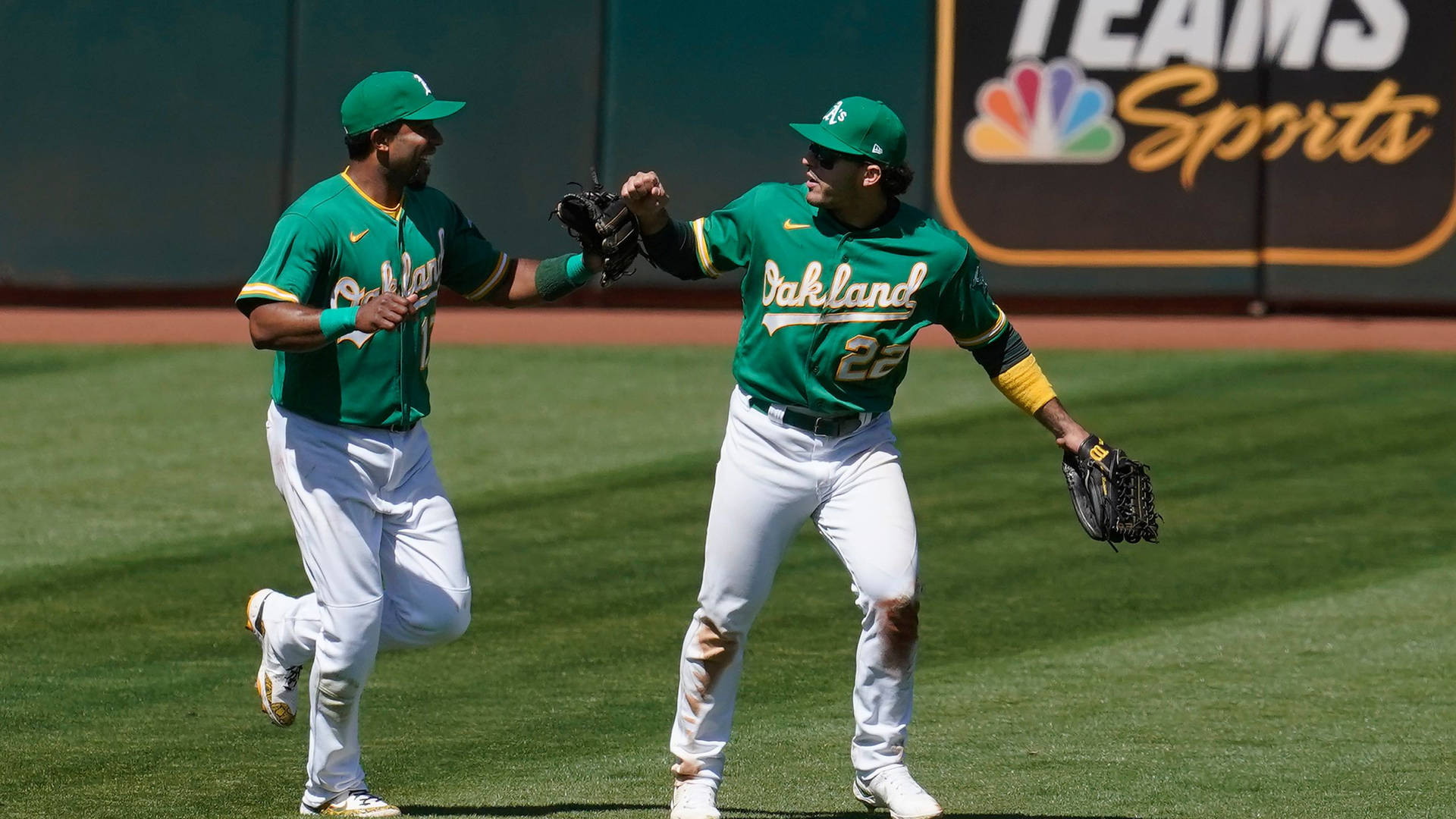 兩名身穿綠色球衣的棒球選手在陽光明媚的球場上擊掌。 — MLB 壁紙