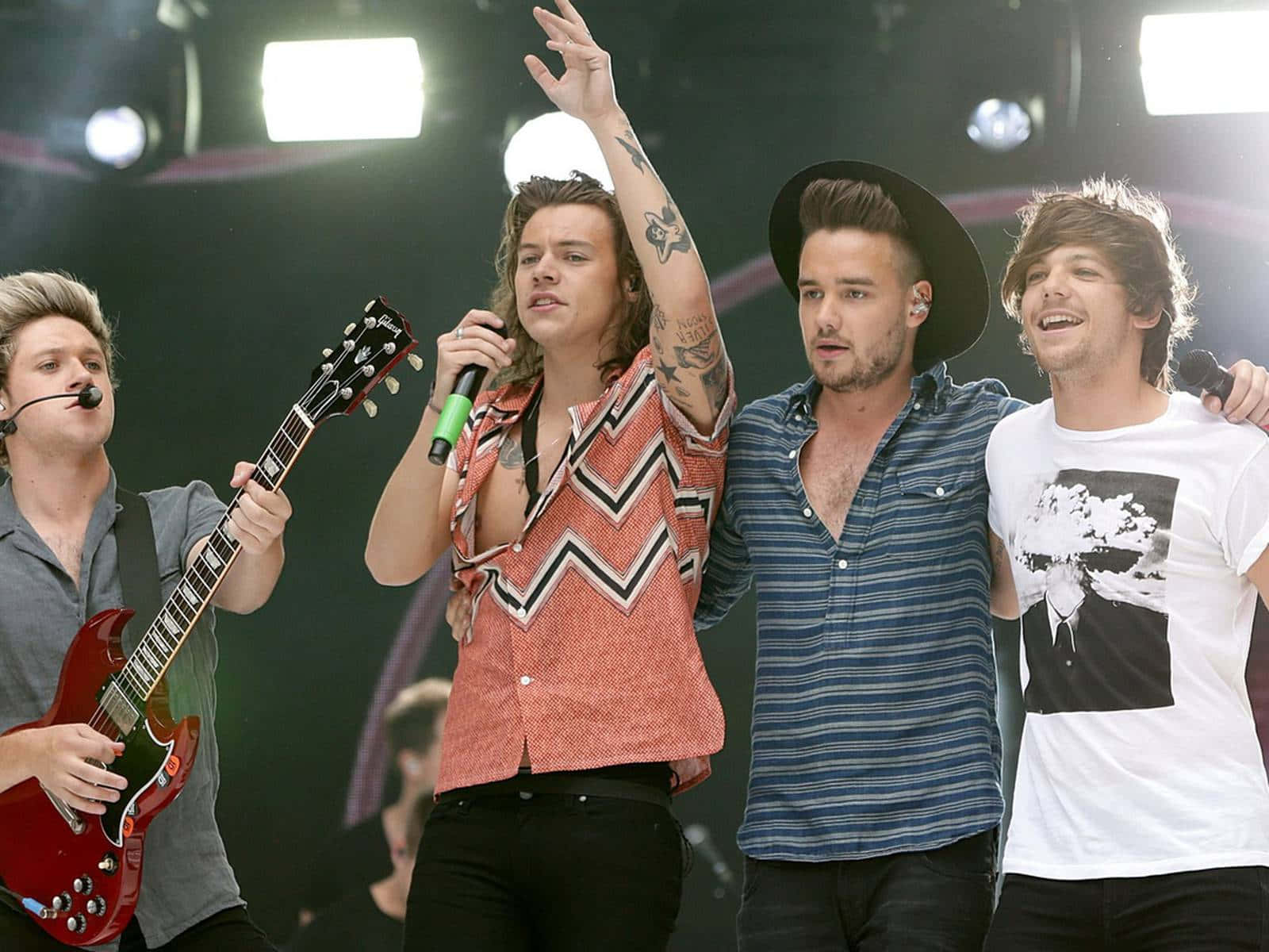 One Direction 桌布 壁紙 — One Direction 在明亮的舞台燈光下，帶著吉他和麥克風充滿活力地表演。