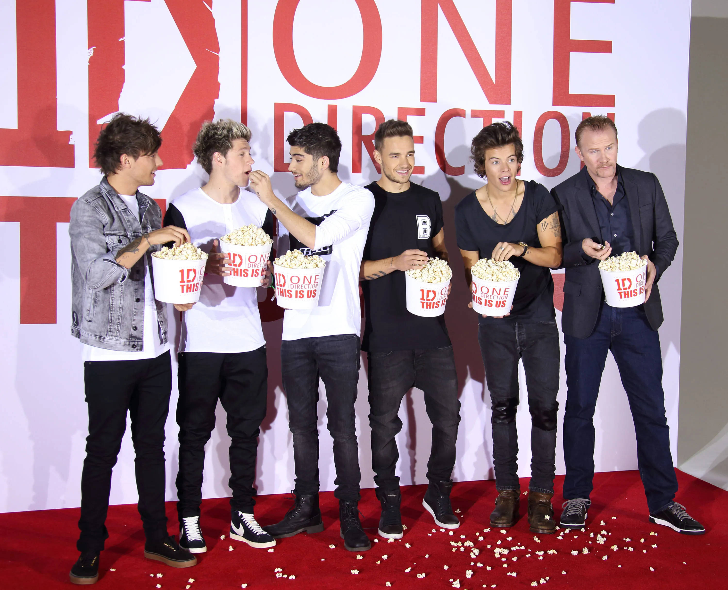One Direction Aesthetic 桌布 壁紙 — One Direction 樂團成員在大型「1D」背景前的紅地毯上大笑並分享爆米花。