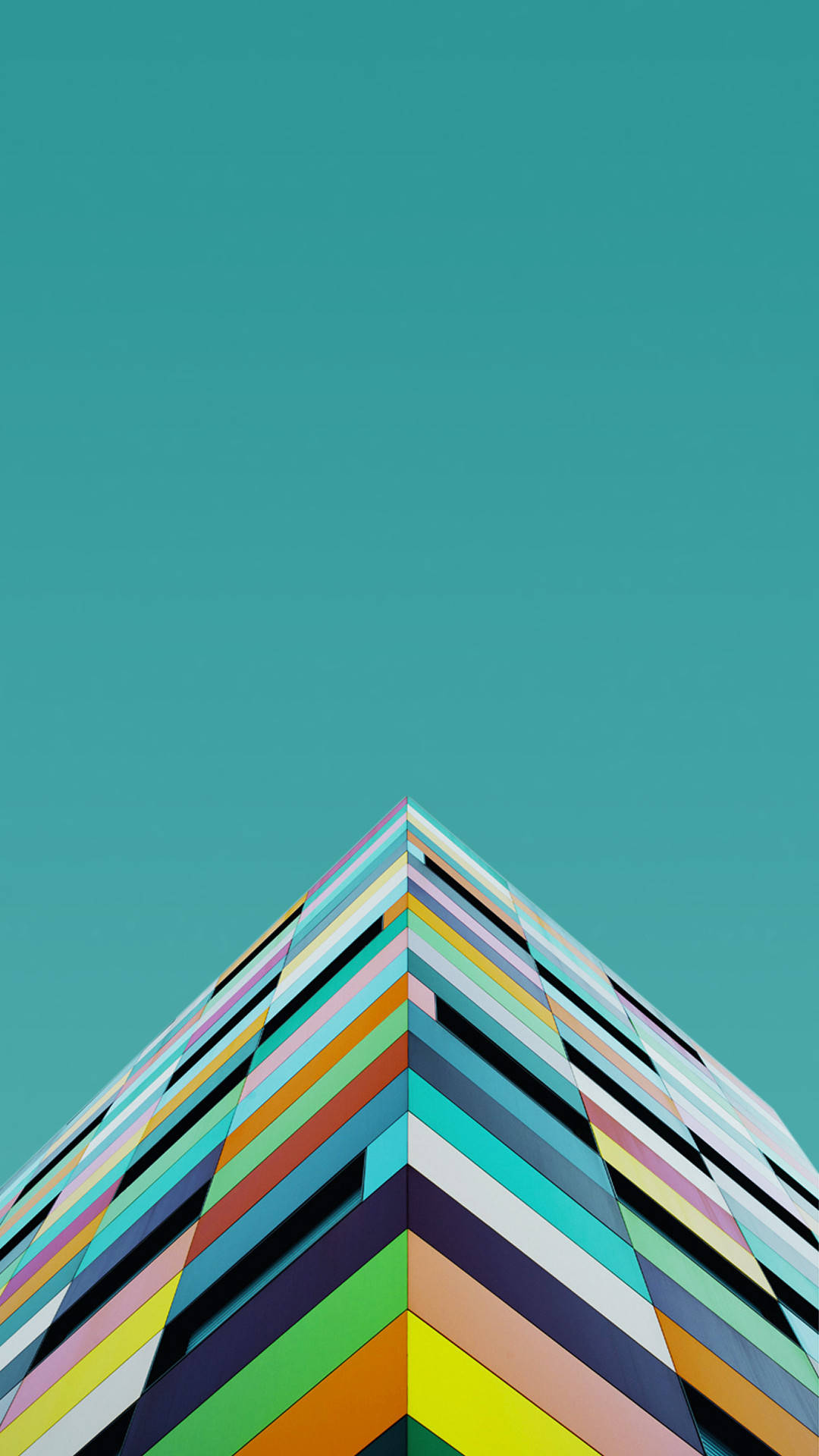 OnePlus 積木邊緣 壁紙 — 一個充滿活力的幾何建築角落，帶有彩虹條紋，在純粹的青綠色天空襯托下聳立。