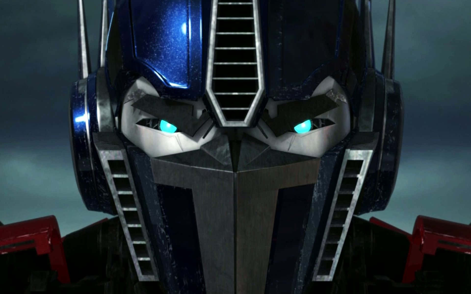 變形金剛 桌布 壁紙 — Optimus Prime 裝甲面部的特寫，藍色眼睛發光，背景是暴風雨的灰色天空。