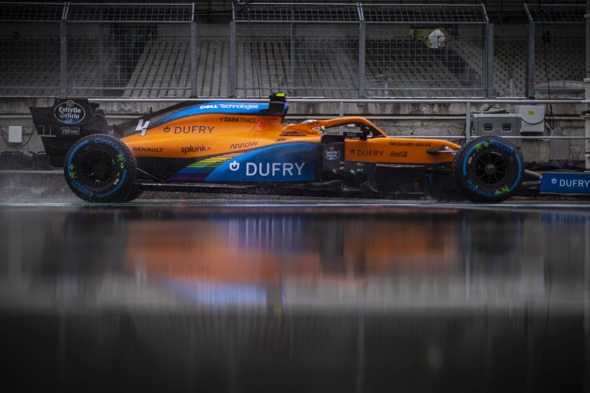橙藍色一級方程式賽車在潮濕賽道上飛馳，帶有倒影 — F1 壁紙