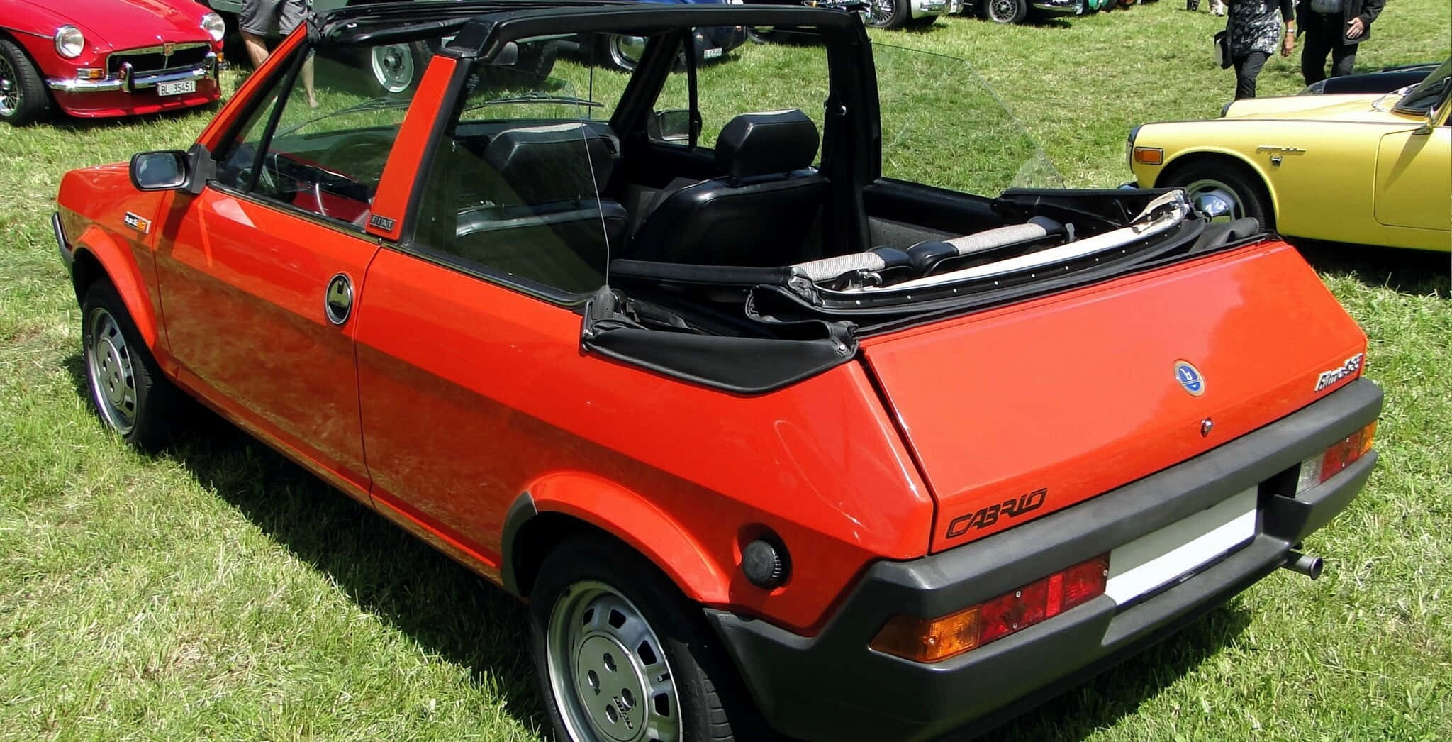 Fiat Ritmo 桌布 壁紙 — 一輛鮮豔的橙色菲亞特敞篷車停放在經典車展的綠色草地上，附近還有其他復古車輛。