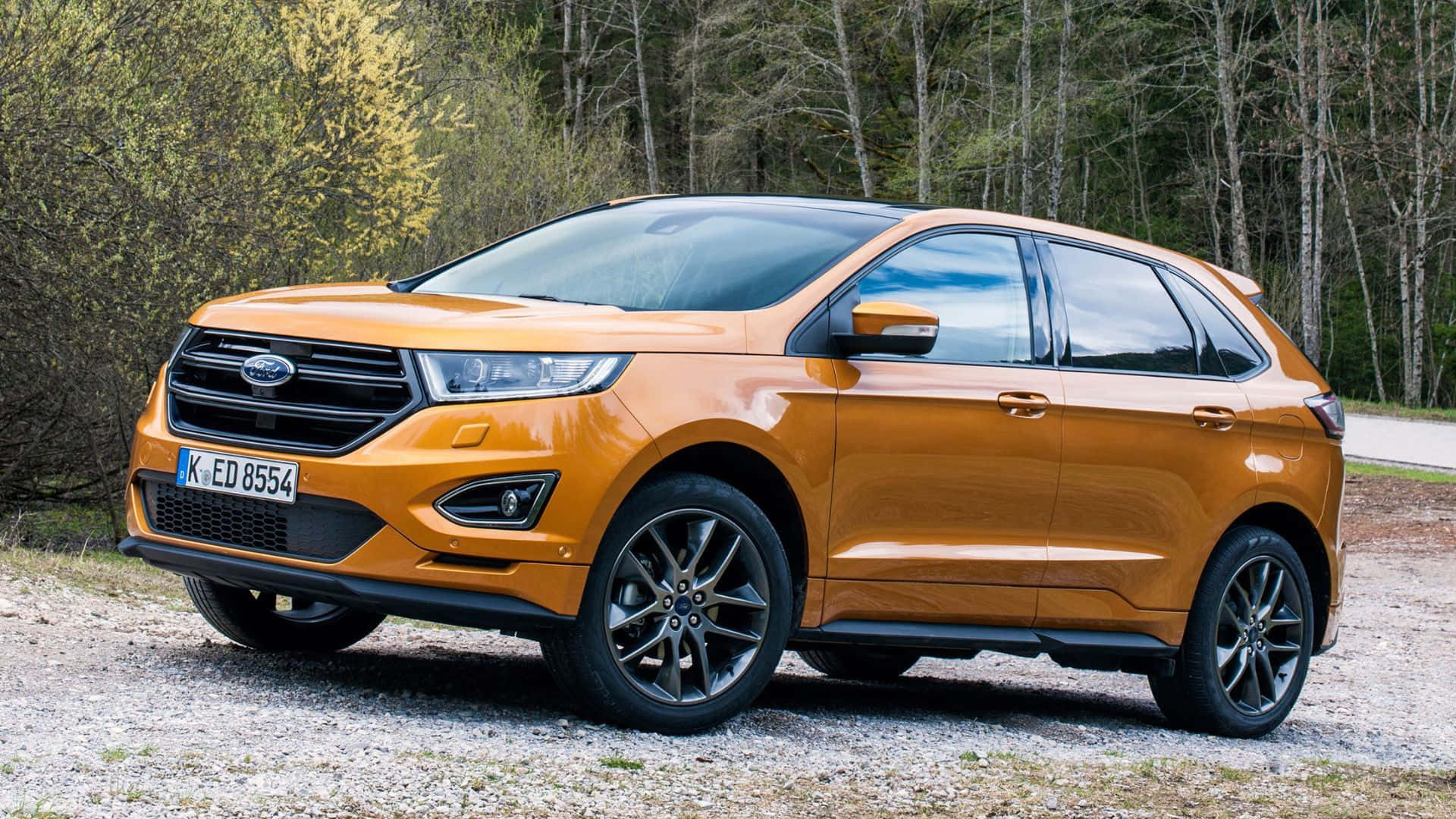 Ford Edge 桌布 壁紙 — 一輛鮮橙色的福特Edge SUV停在碎石上，背景是森林，在明亮的日光下。
