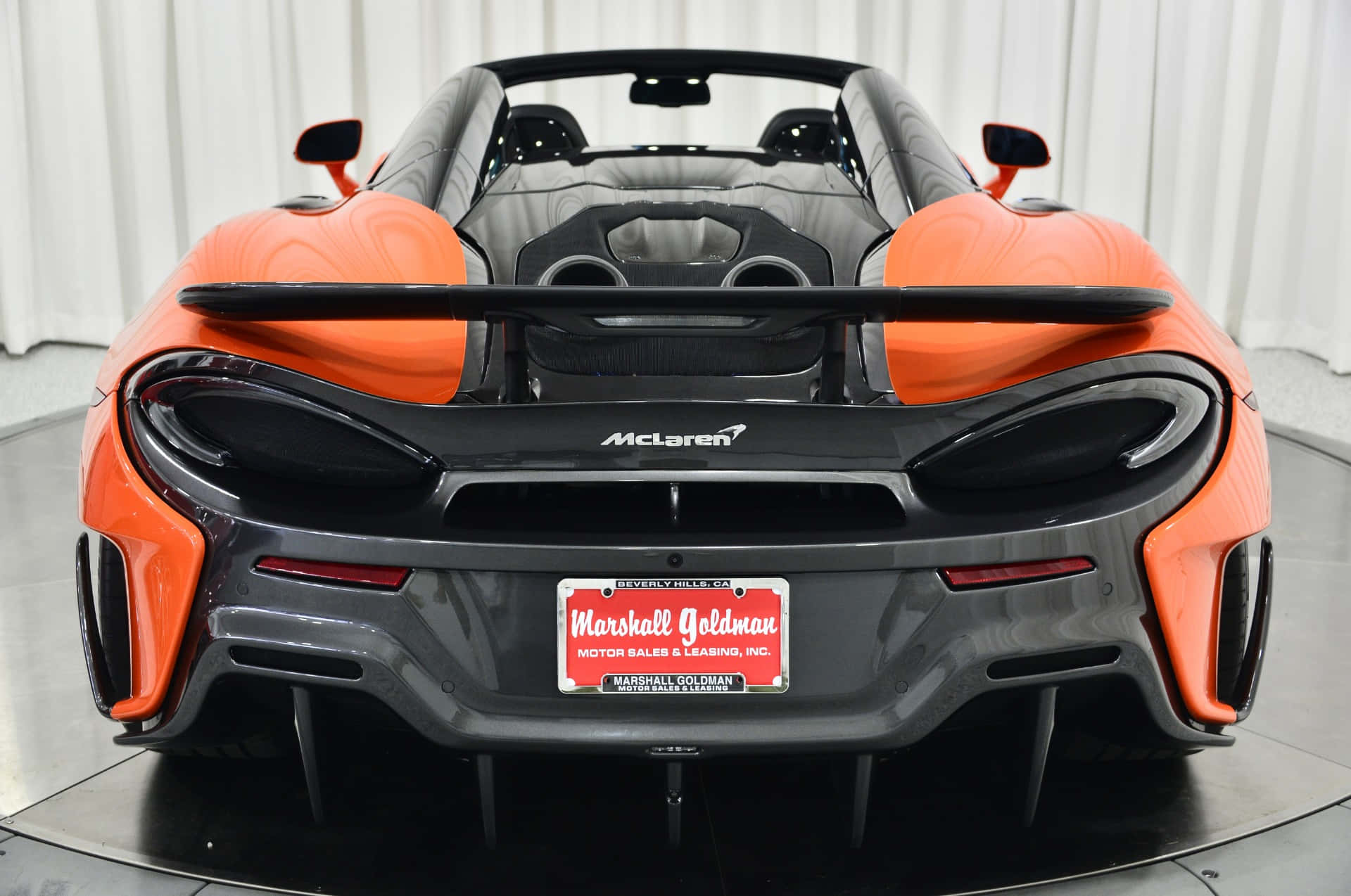 Mclaren 600lt Spider 桌布 壁紙 — 在工作室環境中展示的鮮橙色McLaren 600LT Spider後視圖，帶有黑色飾邊和自訂車牌。