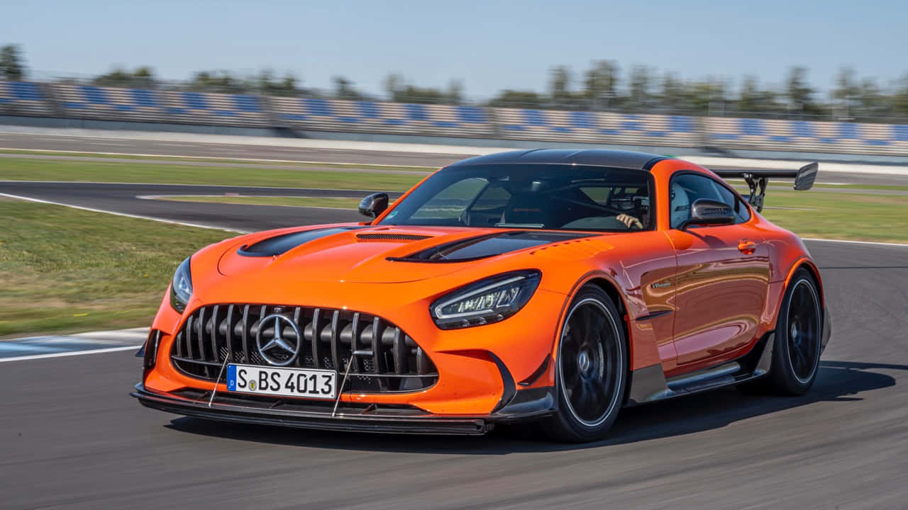 Mercedes Benz Amg Gt 桌布 壁紙 — 一輛鮮橙色的Mercedes-AMG GT R賽車在陽光明媚的賽道上疾馳，背景有模糊的動態和藍白相間的護欄。