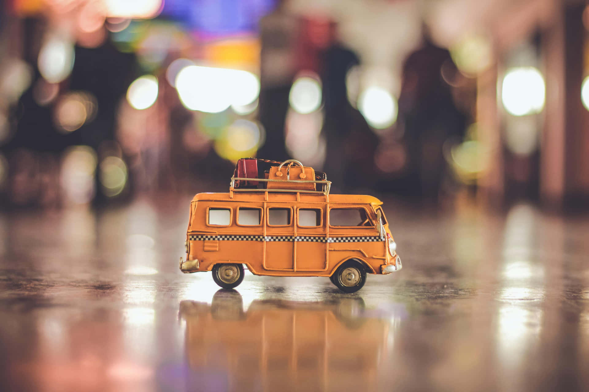  壁紙 — 一輛迷你橙色露營車連同行李放在光亮的地板上，反射出夜晚模糊的城市燈光。