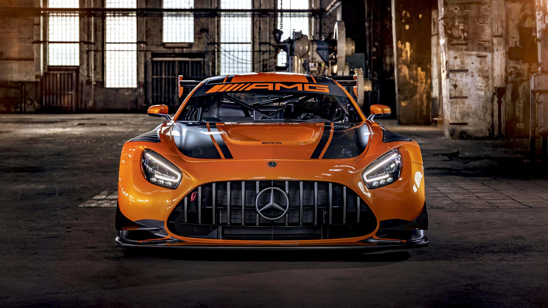 橘色 Mercedes-AMG GT3 賽車停放在陽光照射的廢棄倉庫中。 — 汽車 4K 壁紙