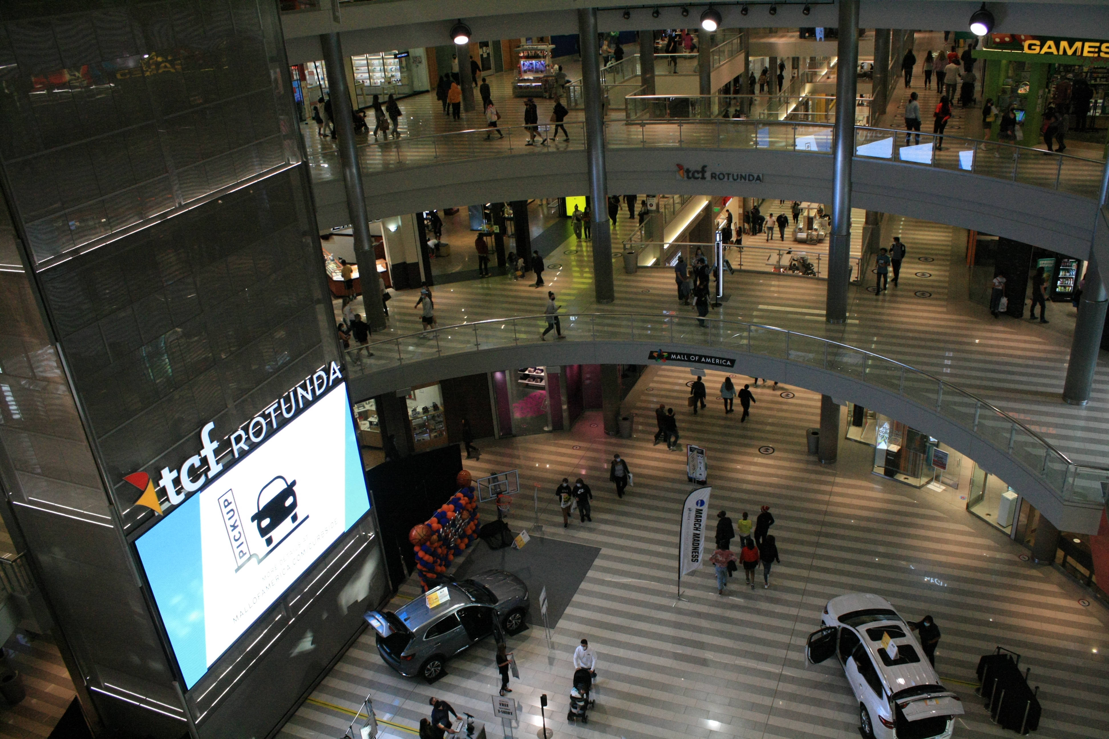Floor Tiles 桌布 壁紙 — Overhead view of a bustling multi-level shopping mall with shoppers walking between levels and cars displayed on the ground floor.