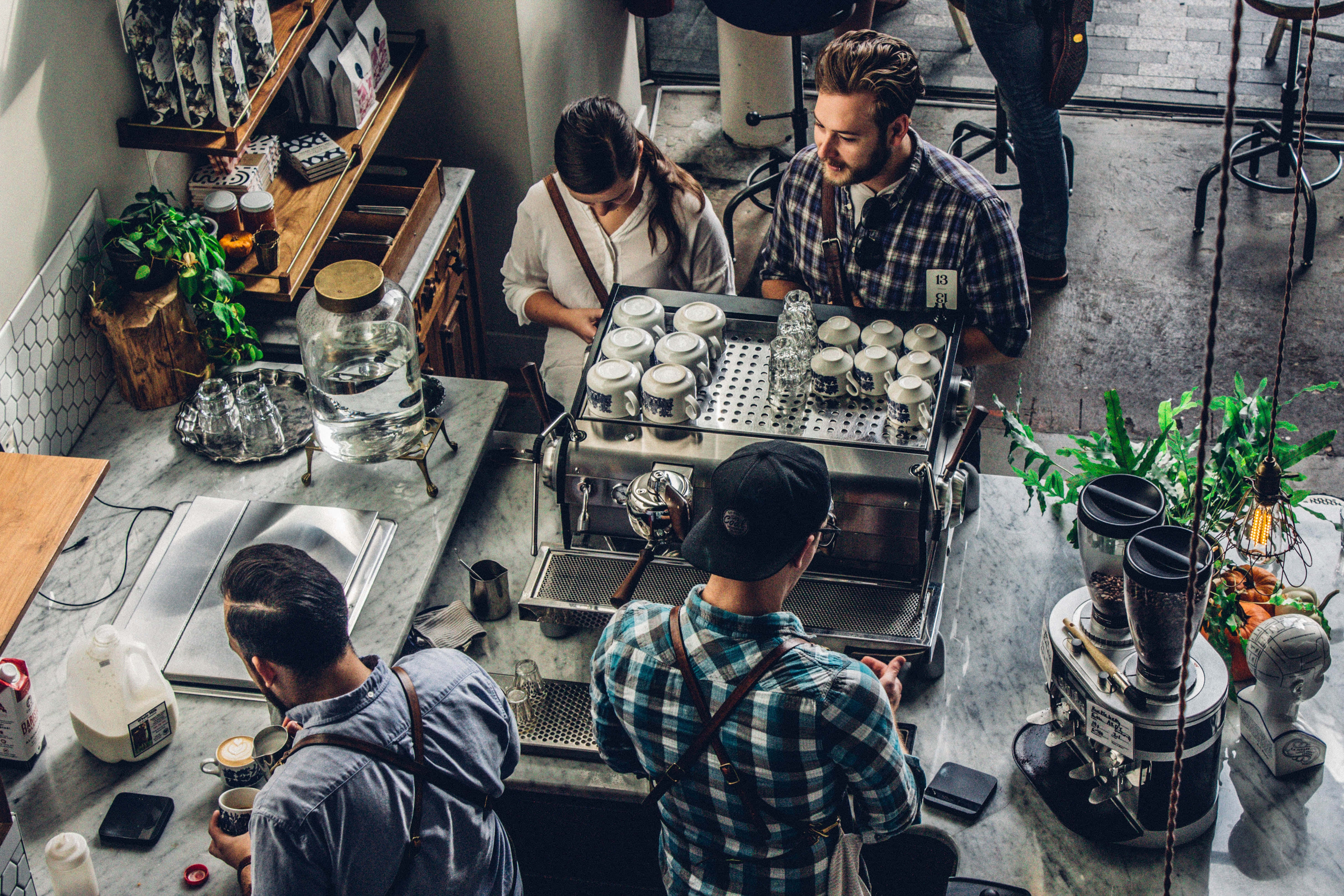 Customer 桌布 壁紙 — Overhead view of baristas and customers at a bustling modern coffee shop with marble counters and green plants.