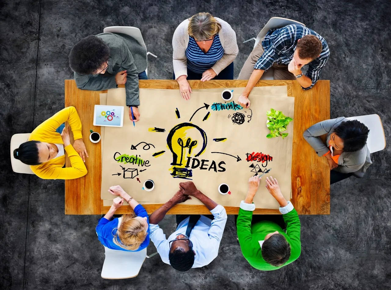 Employee 桌布 壁紙 — Overhead view of diverse team brainstorming creative ideas around a wooden table with a large lightbulb sketch.