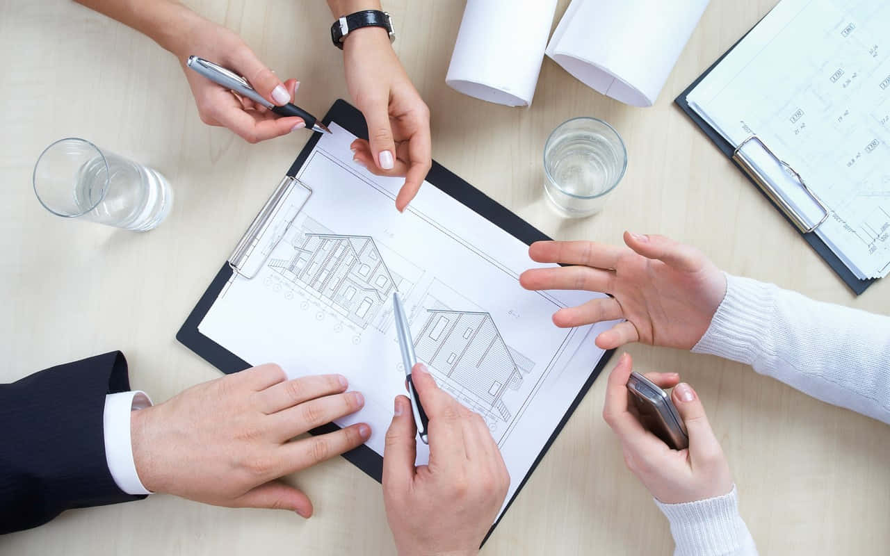 房屋 桌布 壁紙 — Overhead view of four people collaborating around a desk reviewing architectural blueprints with pens and glasses of water.